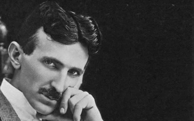 A black-and-white portrait photograph of a mustached man resting his chin on his hand, looking thoughtfully at the camera.