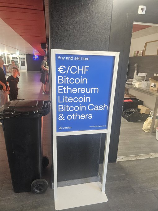 A sign for the cryptocurrency exchange Värdex reads 'Buy and sell here €/CHF Bitcoin Ethereum Litecoin Bitcoin Cash & others' in an indoor setting.