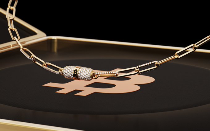 A close-up product shot of a gold-toned necklace with a pavé clasp resting on a black tray that displays a rose-gold logo.