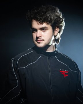 A young man with curly hair and a light beard poses in a dark navy jacket featuring a red esports team logo (FaZe Clan), likely representing the CS:GO player Broky amid discussions about his team status and future roster prospects.
