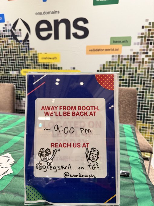 A handwritten sign at an ENS (Ethereum Name Service) booth reading 'AWAY FROM BOOTH, WE'LL BE BACK AT ~9:00 PM. REACH US AT @ogbegskril on TG. @workcemon.'