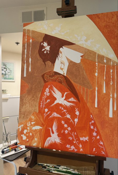 A painting on an easel depicting a figure in flowing orange robes with white cranes, featuring hanging tassel decorations against a warm orange and gold background.