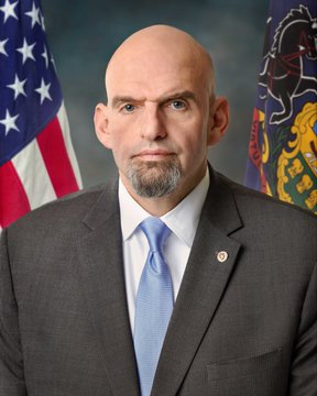 The image depicts a bald man wearing a suit standing in front of two American flags, one of which features a horse emblem along with the words "U.S." This suggests that he might be representing an organization or government involved in matters related to national symbols or patriotism.