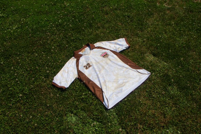 A white and brown sports jacket with the number '27' and a small emblem lies spread out on green grass.