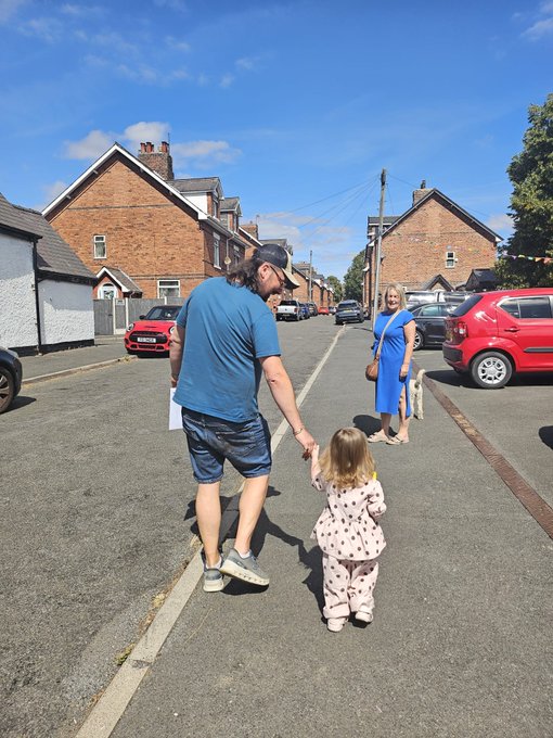 A man in a blue shirt and cap walks down a residential street holding the hand of a small child in a white polka-dot outfit, while a woman in a blue dress approaches from the opposite direction. The image evokes the "Early start, earlier opportunities" and "Go Get money" spirit, symbolizing family and forward momentum toward financial goals.