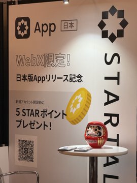 A promotional display for STARAL App in Japan, featuring 'WebX限定!' text, '5 STARポイント プレゼント!' offer, a QR code, and a Daruma doll on a pedestal.