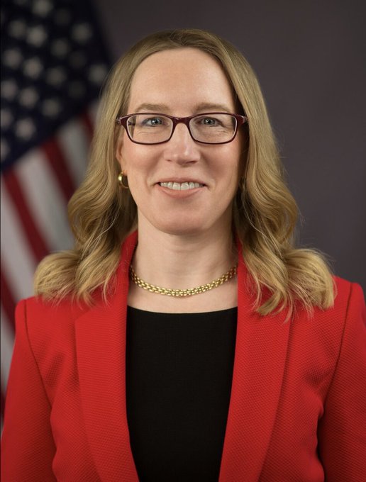 A professional portrait shows a woman with blonde hair, wearing a red blazer over a black top, glasses, and a gold necklace, smiling in front of an American flag backdrop. The image accompanies a post about SEC Commissioner Hester Peirce, suggesting she is pictured here delivering remarks on how federal securities laws still apply to onchain lending and vaults involving investment contracts.