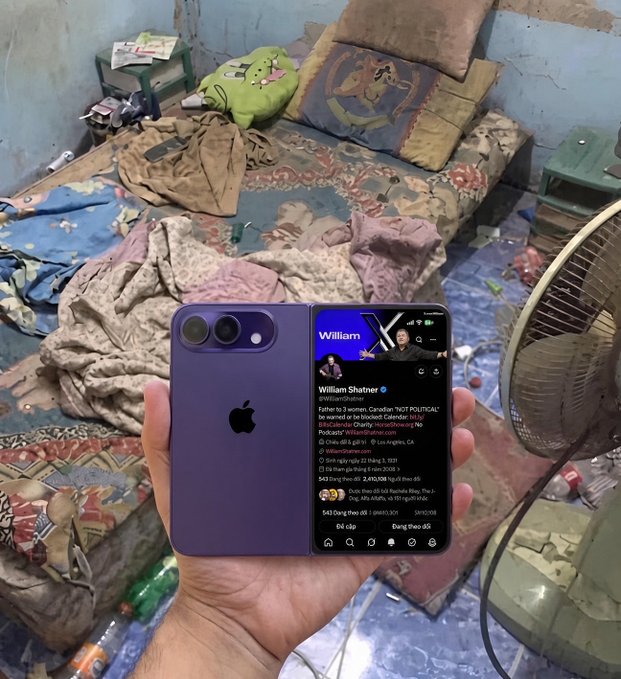 A hand holds a purple iPhone displaying the X (Twitter) profile of William Shatner (@WilliamShatner) with a verified tweet, set against a backdrop of a cluttered room with a bed and standing fan.