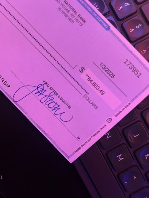 A check from National Bank of Las Vegas, NV dated 1/3/2025 for $64,603.49 with check number 173951, resting on a backlit keyboard with purple lighting. The check is made out 'VOID AFTER 6 MONTHS' and has a signature.