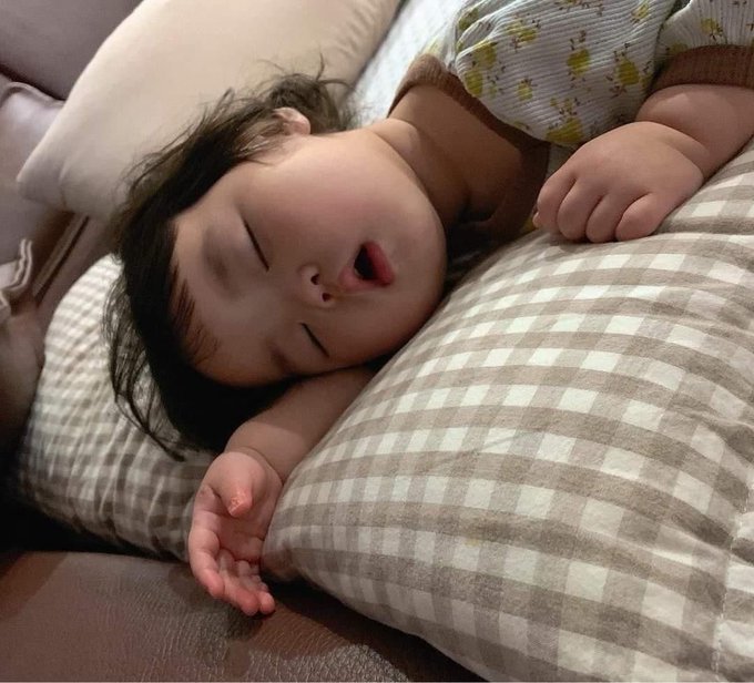 A young child sleeps peacefully on a checkered pillow with their mouth slightly open. The peaceful slumber captures the cozy, restful mood of wishing followers a good night and sweet dreams.