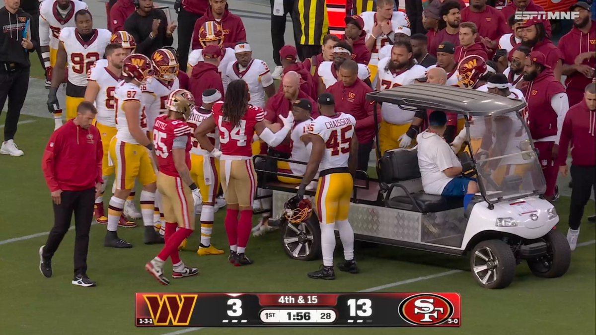Commanders players and medical staff gather around a medical cart on the field, with player #54 visible holding a helmet while #45 (Chaisson) looks on. The scoreboard at the bottom shows the 49ers leading the Commanders 13-3 in the 1st quarter with 1:56 remaining and a 4th & 15 situation, consistent with the moment Terry McLaurin was carted off with an apparent knee injury.