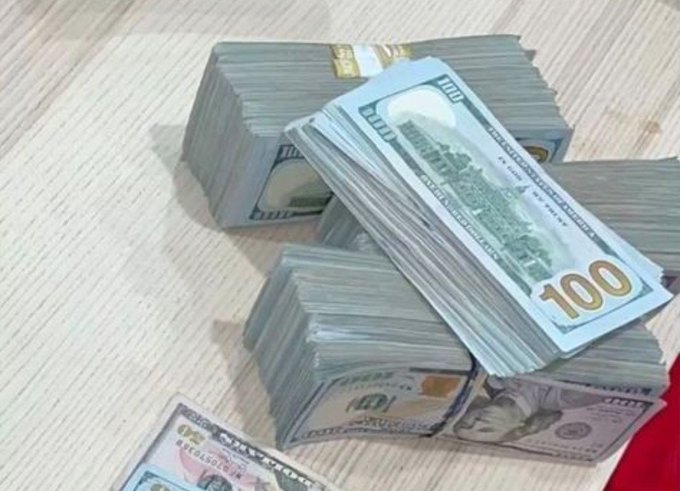 Multiple stacks of $100 US bills bundled together sit on a wooden surface, reinforcing the post's message about hustling to make money on your own. The prominent "100" text on the bills emphasizes the value of pursuing financial independence without relying on others.