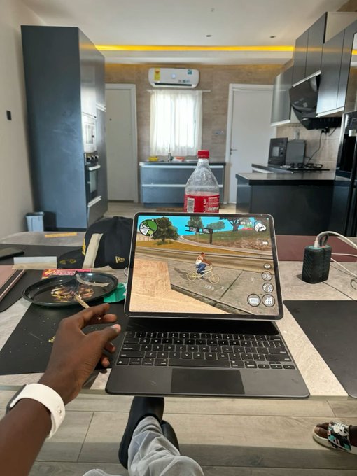 A person using an iPad showing what appears to be a skateboarding video game, with a bottle of Coca-Cola on a table in a modern kitchen setting.