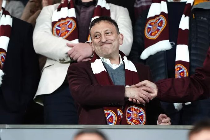 A smiling man in a maroon jacket and matching Heart of Midlothian F.C. scarf (marked "HMFC 1874") shakes hands with someone off-camera while surrounded by other fans wearing identical scarves, reflecting the post's sentiment that the club is consistently on everyone's minds entering its second year of notable prominence.