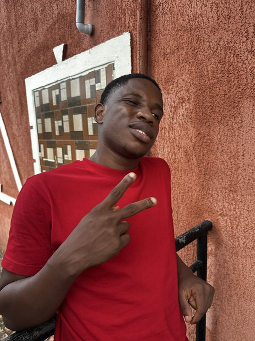 A young man in a red t-shirt flashes a peace sign with a relaxed smile while standing against a textured reddish wall. The casual, upbeat selfie complements the "Gm CT" (Good morning Crypto Twitter) greeting and sets a friendly tone for the promised market content and alpha.