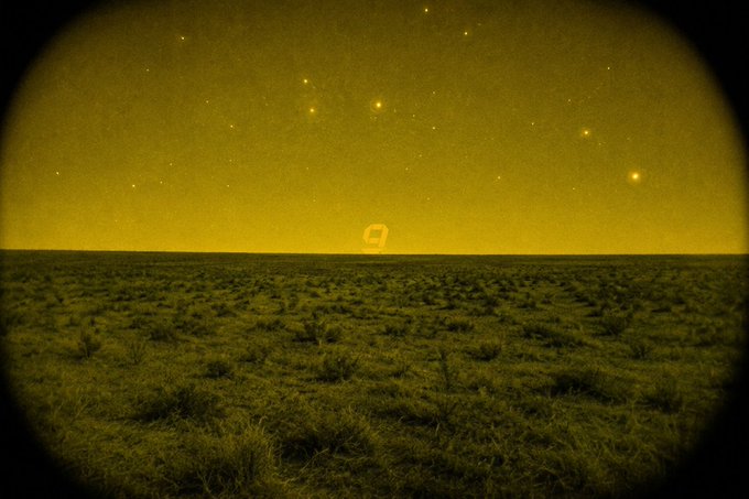 A sepia-toned image viewed through a circular lens shows a barren landscape under a starry sky, with a small figure visible on the horizon.