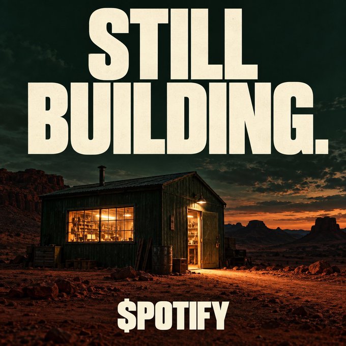 A stylized advertisement showing a small illuminated wooden cabin in a desert landscape at sunset with bold text 'STILL BUILDING.' and the Spotify logo.