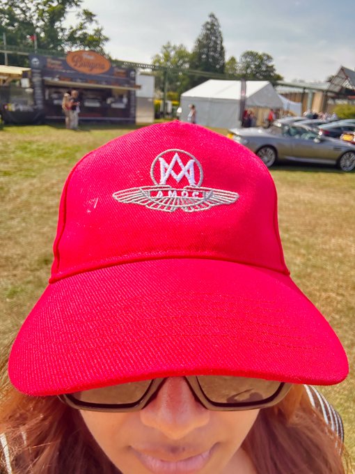 urn of gold and white flowers, a red baseball cap with "M" and "P" logo, sunglasses, and a car on the side of the road.