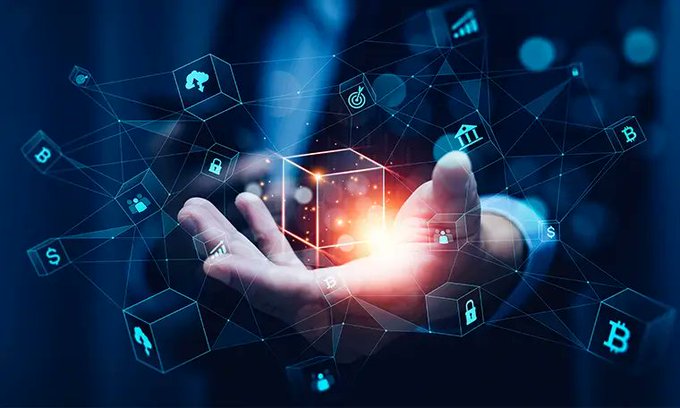 A person in a suit holds out their hand beneath a glowing holographic cube, surrounded by floating blue icons representing cryptocurrency, finance, and digital security.