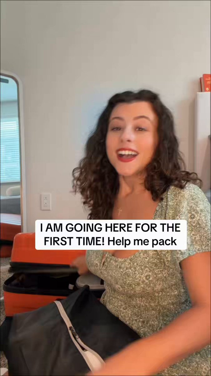 The image features a woman sitting down with her luggage, smiling as she looks directly into the camera. The suitcase next to her has a "Help me pack for my first trip to Europe!" sticker on it, indicating that she might be preparing for an upcoming journey or just returning from one.