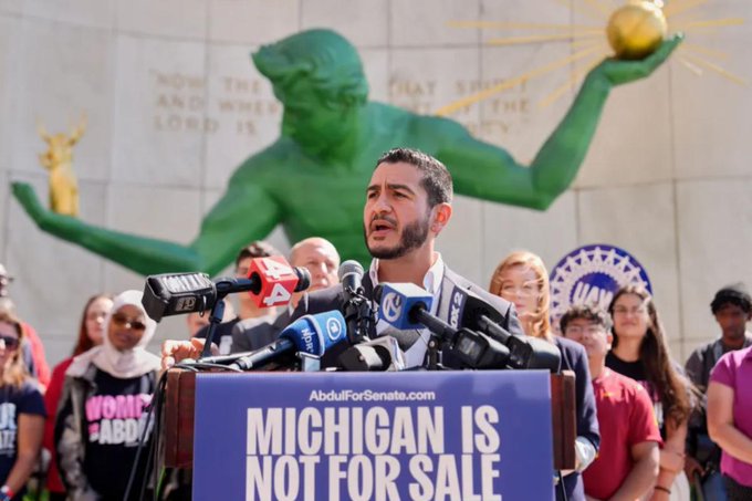 A man speaks at a podium labeled 'MICHIGAN IS NOT FOR SALE' with 'AbdulForSenate.com', standing in front of the Spirit of Detroit statue.