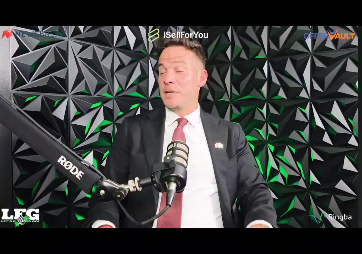 The image features a man wearing a suit, sitting behind a microphone with his hands on his lap while speaking into it. He appears to be giving a speech or presentation about Bitcoin, as indicated by the text "Bitcoin Nfts on bitcoin is going to be the next biggest thing". The man's attire and the content of his speech suggest that he might be discussing the potential impact of Bitcoin on the financial world or sharing insights about its future development.