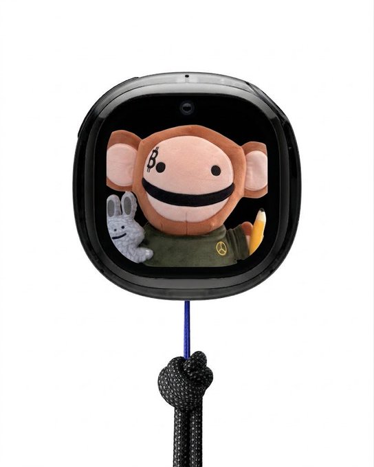 A black smartwatch-style digital pet device displays a stuffed monkey character, with a small bunny and what appears to be a banana visible on the screen.