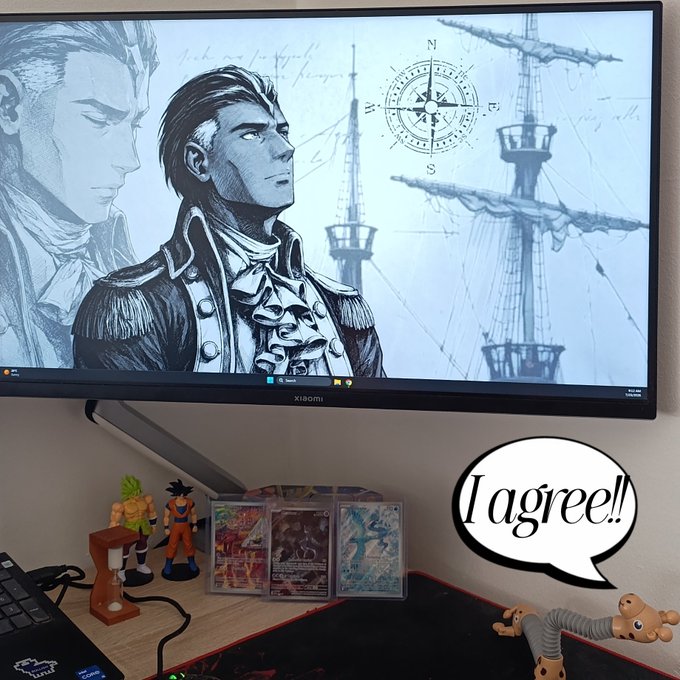 A Xiaomi monitor displays a sketch of a naval officer in front of a ship's mast and compass; below it are anime figurines, trading cards, and a speech bubble reading 'I agree!'.