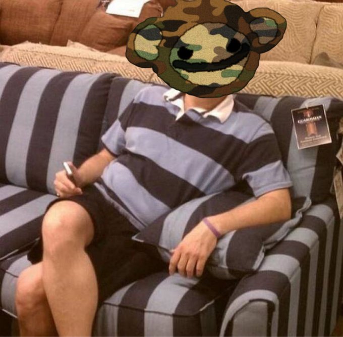A casual photo of a person sitting on a striped couch wearing a striped polo shirt and shorts, with a cartoon camouflage bear face emoji covering their head, and a 'Chamrosh' lanyard visible in the background.