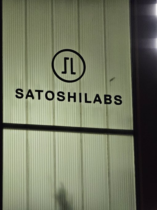 A logo featuring a stylized 'SL' monogram inside a circle with the text 'SatoshiLabs' displayed on a green textured glass or screen surface.