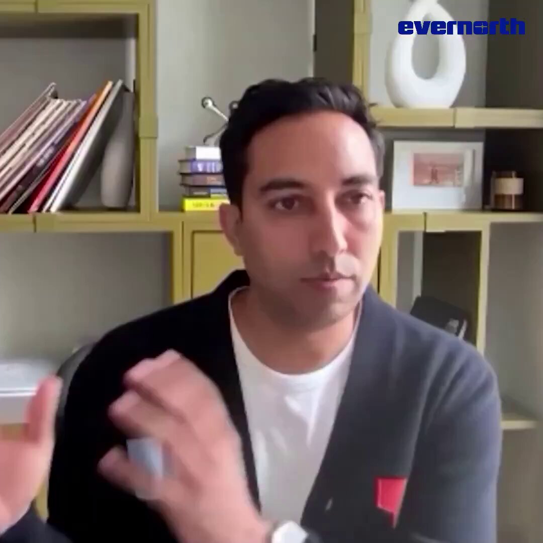 The image features a man wearing a black jacket, sitting at a desk surrounded by bookshelves filled with various items such as vases and records. The man appears to be engaged in a conversation or presentation related to Ripple, XRP, or blockchain technology. The background includes a white wall adorned with multiple bookshelves, suggesting that the setting could be an office or a workspace where discussions about these topics might take place.