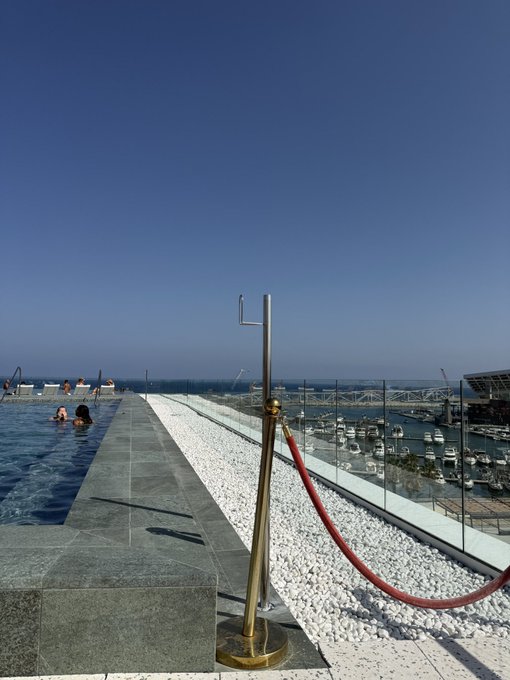 A rooftop infinity pool overlooks a marina filled with boats under a clear blue sky. This serene scene contrasts with the author's anxiety about interacting with locals in Barcelona due to its reputation for pickpocketing.