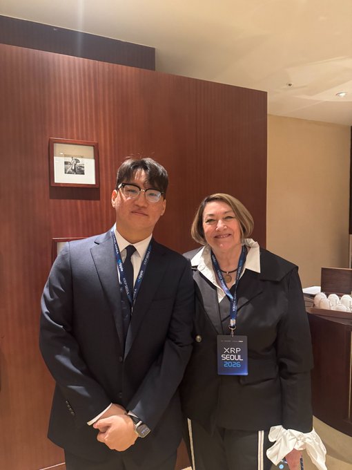 Two people in business attire pose together at the XRP Seoul 2025 conference, wearing 'XRP SEOUL 2025' lanyards.