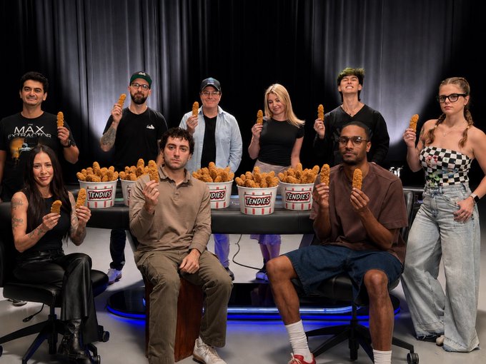 A group of nine people pose around a table filled with buckets labeled "TENDIES," each holding a fried chicken tender, matching the post's reference to the trending $TENDIES cryptocurrency running on CT (Crypto Twitter).