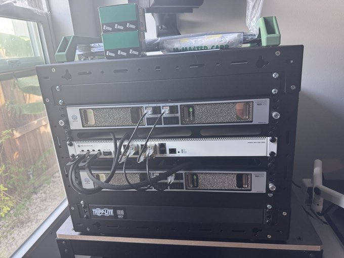 A Tripp Lite server rack setup containing various networking equipment including routers and access points, positioned near a window with green cables on top.