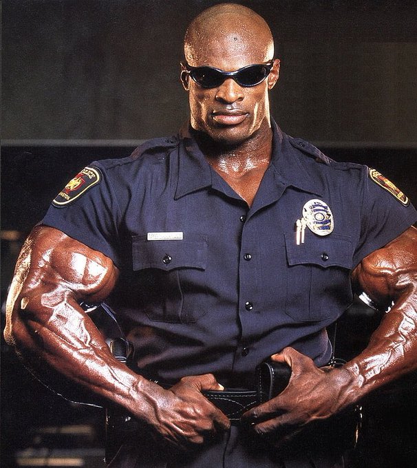 A muscular man in a police uniform with sunglasses, sweating, with highly defined arm muscles.