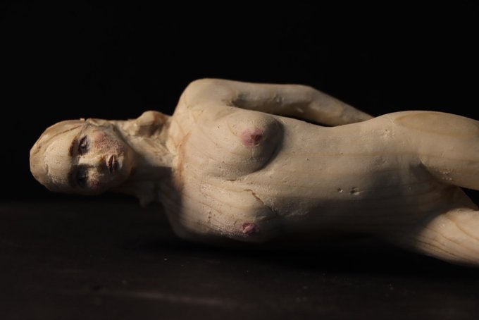 A photograph of an unfinished clay sculpture depicting a reclining female figure, showing the raw material and structural armatures on a dark surface.