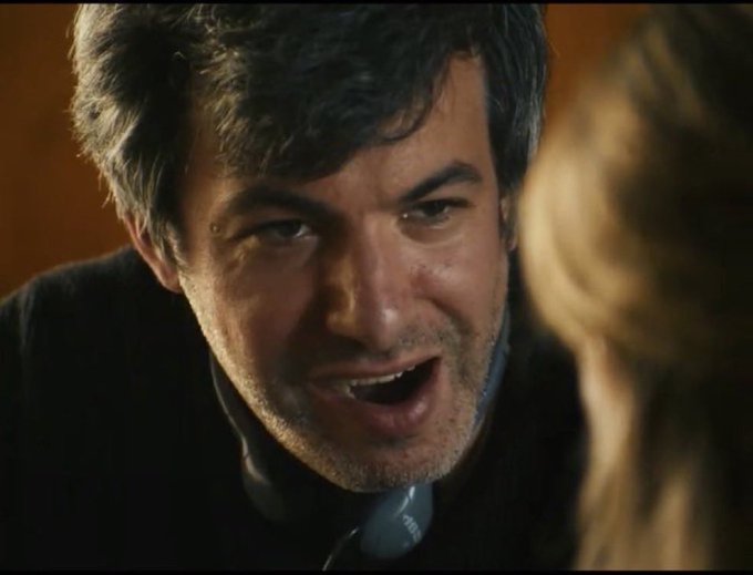 A close-up shot of a man holding a phone to his ear with a strained, exasperated expression on his face, his mouth open as if yelling or arguing. His frustrated demeanor perfectly captures the feeling of someone overhearing ridiculous claims about Bitcoin plummeting to $40k while on a phone call.
