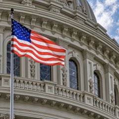 The U.S. flag flies prominently in front of an ornate government building, likely the U.S. Capitol, symbolizing the legislative action at the heart of the news about Republican senators' warnings that the Senate crypto market structure bill may fail next week over unresolved ethics provisions.