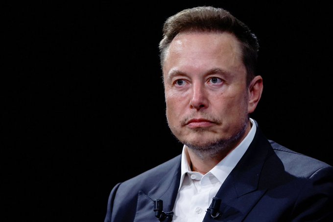 The image features a man, possibly an actor or speaker, standing against a black background with his head tilted slightly to the side. He appears to be in a reflective or thoughtful pose. The caption above the picture provides more information about the context behind this image and its relevance to the original post discussing Tesla CEO Elon Musk's recent speech at a conference. The caption reveals that the speech was made as part of the Tesla Lands Space Force contract, which is worth around $2.29B US defense contracts. Additionally, Bitcoin was also mentioned in relation to the space-based data network being constructed by the company.