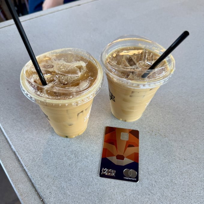 The image shows two styrofoam cups filled with iced coffee sitting on a table next to each other. A credit card is placed between the cups, suggesting that someone has paid for their drinks using the card. The text "Afternoon coffee by @MetaMask" indicates that this was taken during the afternoon hours and the person who took the photo likely used social media to share the moment with others.

The post also mentions a credit card payment made directly into a My Keys, my coins, my coffee account. This implies that the person paid for their drinks using an online payment method or mobile wallet app, which is supported by the credit card in question. The image captures a casual and relaxed atmosphere as people enjoy their afternoon coffee together.