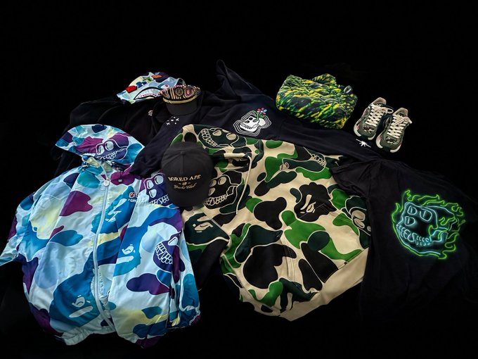A collection of streetwear items, including camouflage jackets, a black cap, and sneakers, is arranged on a black background with 'World App' visible on a tag.