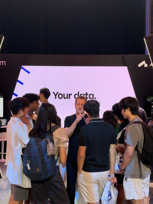 A presenter gestures while engaging with a crowd of attentive attendees in front of a large screen displaying "Your data." at what appears to be the Walrus booth, with attendees testing demos as referenced in the Singapore event post.