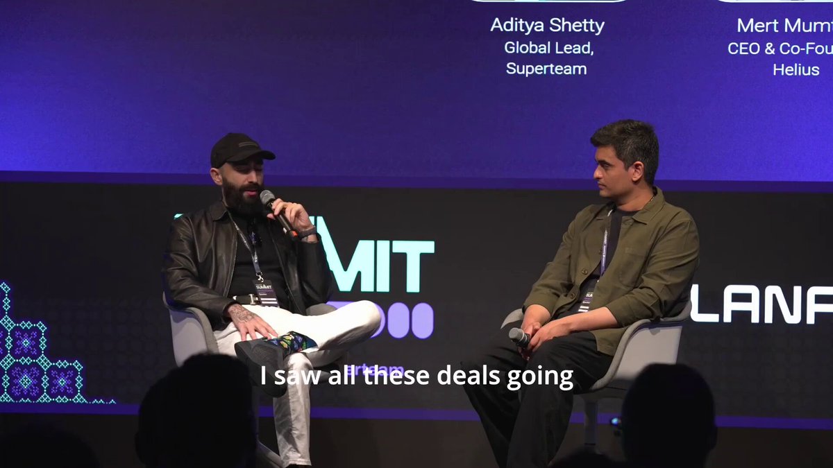 The image shows two men sitting next to each other at a conference or event, with one man holding a microphone while the other has his hands crossed. They appear to be engaged in conversation about a topic related to Helius, as indicated by the caption "at Solana Summit Germany, @mert talked about why Helius acquired Light Protocol". The image also includes text that reads "I saw all these deals going" and "I saw all these deals going", suggesting that they are discussing various deals or projects happening at the event.