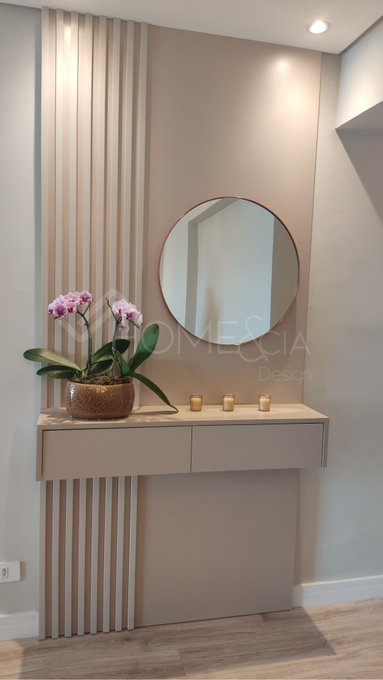 A modern bathroom vanity with a round mirror, gold fixtures, and a pink orchid plant, designed by OMNESIA Design with fluted wall paneling in beige tones.