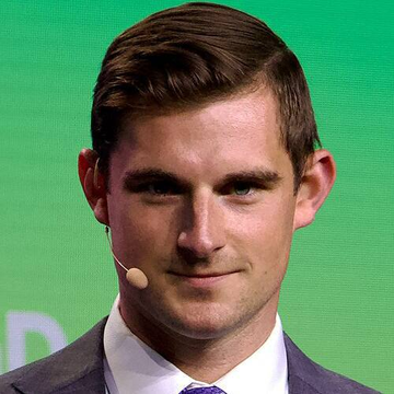 A young man in a dark suit and tie, wearing an earpiece microphone, smiles slightly against a green backdrop. The image accompanies a post quoting Bo Hines, head of Tether's US arm, advising "Never sell your Bitcoin," suggesting he is the speaker pictured at a related event.