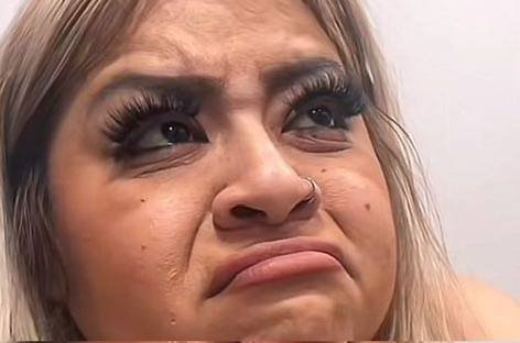 A close-up photo of a blonde woman's face showing an emotional, tearful expression with heavy eyelashes, a nose ring, and a quivering lip.