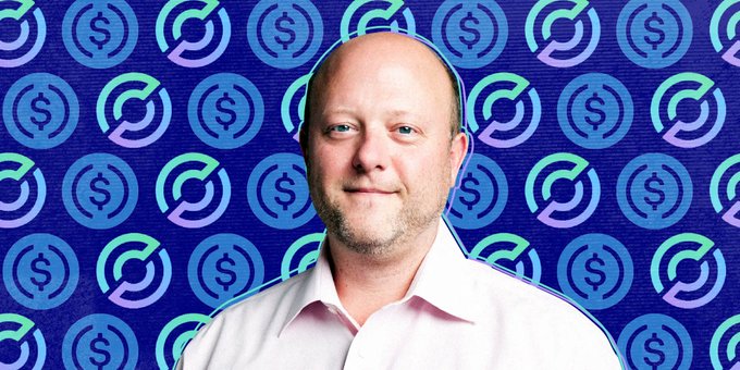 Circle CEO Jeremy Allaire appears in front of a backdrop patterned with USDC dollar logos, as he defends USDC's competitive position against emerging rivals like Open Standard Dollar ($OUSD) following a 16% drop in $CRCL shares.