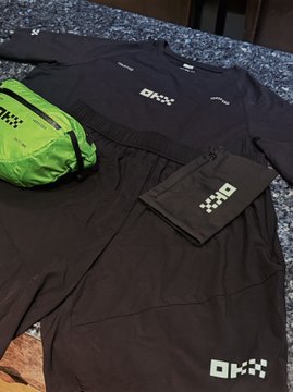 Photo of ORKK-branded athletic apparel laid out on a bed, including black shorts/shirt and a green and black bag.