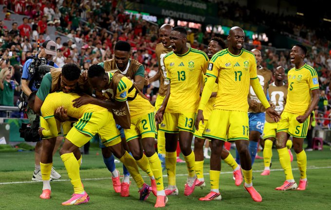 South African national team players, wearing yellow and green kits with visible jersey numbers 13, 17, and 5, celebrate enthusiastically on the pitch in Monterrey during the 2026 World Cup qualifiers. The jubilant scene reflects South Africa's strong performance in a matchup where, despite Canada being favored by traders, the South Africans appear to be controlling the game's run of play.